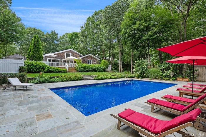 Outdoor pool featuring view of mature landscaping and a patio area
