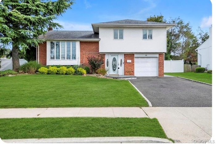 Tri-level home with brick siding, a garage, asphalt driveway, and a shingled roof