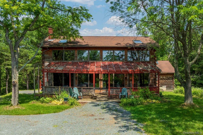 View of front facade with a front yard, a chimney, log exterior, and a shingled roof