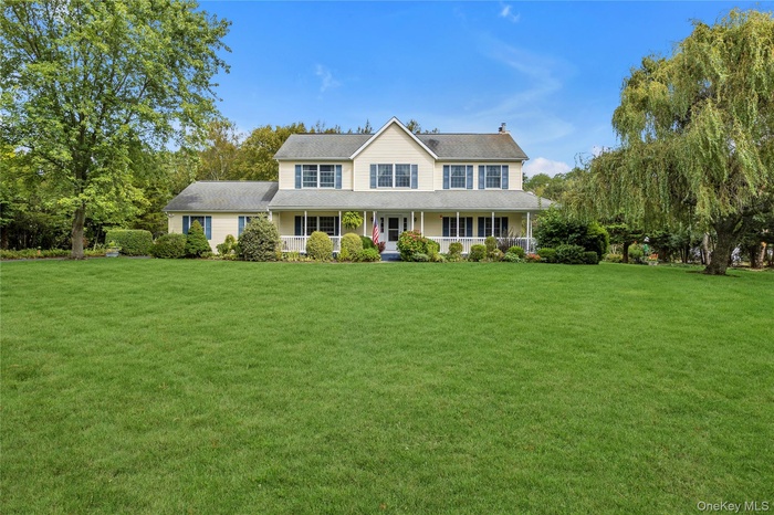 View of front facade featuring a porch, a front yard, a shingled roof, and a chimney