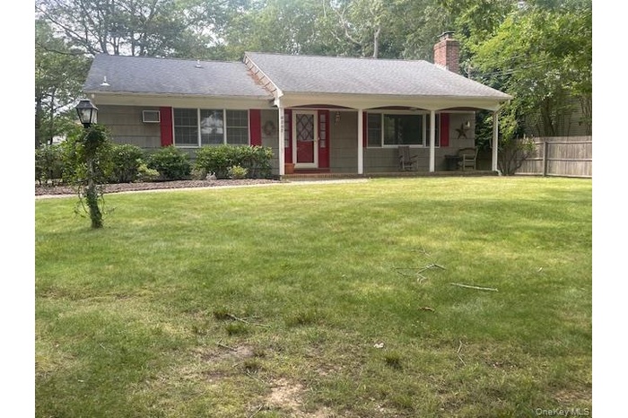 Ranch-style house with covered porch, a chimney, roof with shingles, and view of wooded area