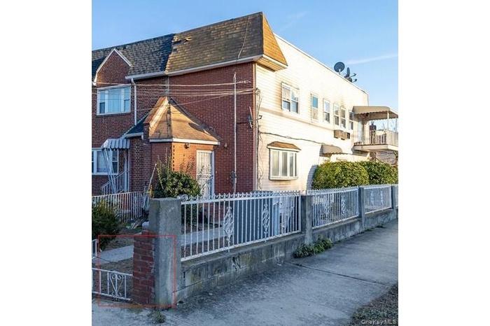 View of side of home with roof with shingles, a fenced front yard, mansard roof, and brick siding