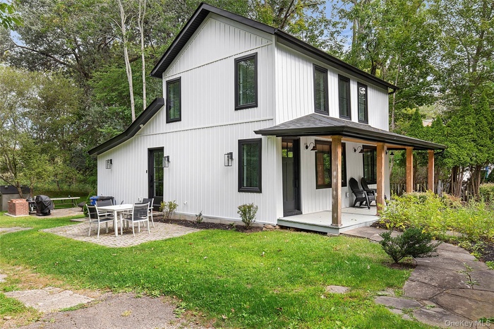 Rear view of house with covered porch, a lawn, view of scattered trees, a patio area, and board and batten siding