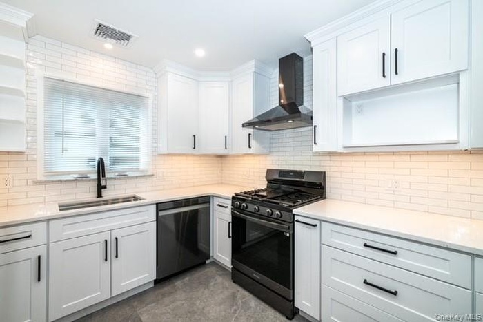 Kitchen with gas range oven, wall chimney range hood, white cabinetry, dishwasher, and tasteful backsplash