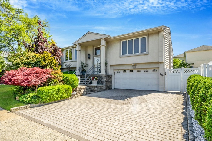 Bi-level home with stucco siding, a gate, an attached garage, and decorative driveway