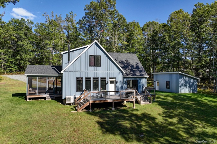 Back of house featuring board and batten siding, roof with shingles, a deck, a lawn, and stairs