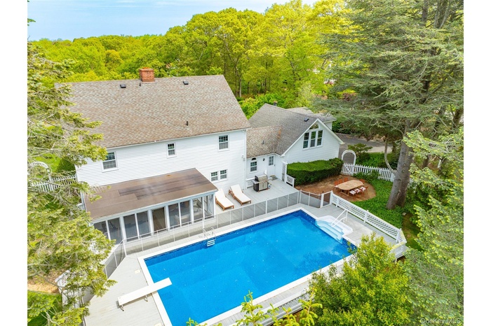 Swimming pool with a sunroom, a fenced backyard, a view of trees, and a diving board