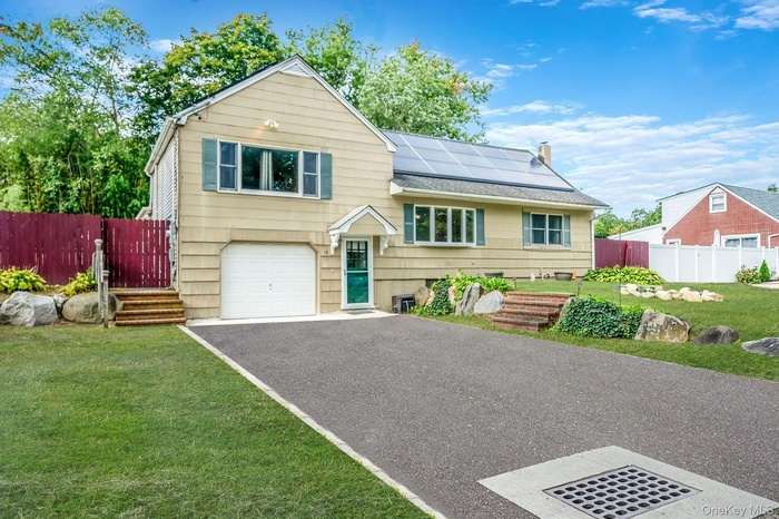 Split level home featuring roof mounted solar panels, asphalt driveway, an attached garage, and rear wood deck