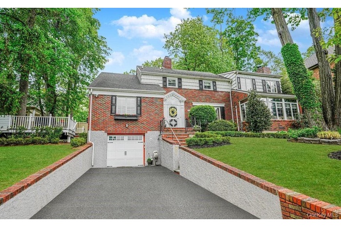 View of front of property with brick siding, a chimney, driveway, an attached garage, and a front lawn