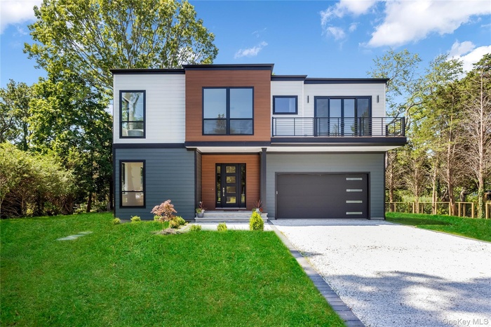 Modern home featuring a balcony, gravel driveway, a front lawn, and an attached garage