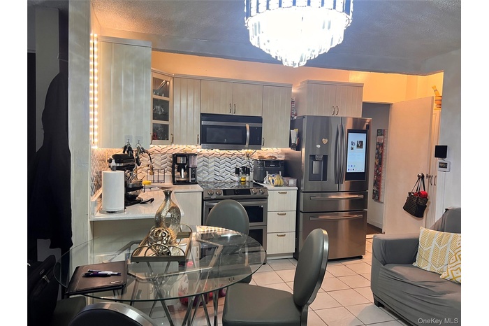 Kitchen featuring a chandelier, a textured ceiling, light tile patterned floors, appliances with stainless steel finishes, and decorative backsplash