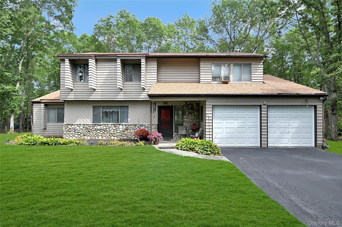 View of front of property with asphalt driveway, a front yard, a shingled roof, and stone siding