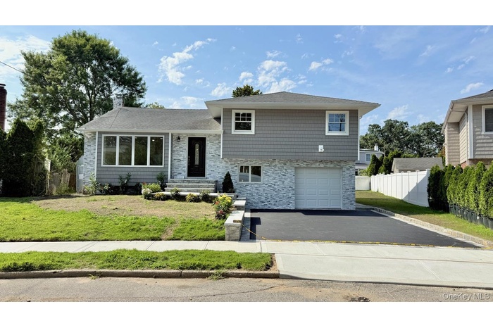 Split level home featuring stone siding, driveway, a chimney, a garage, and a shingled roof