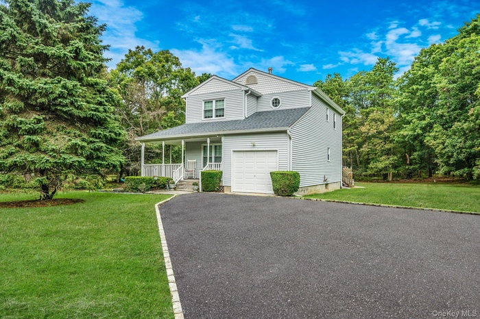 View of front of house with a porch, a front yard, a shingled roof, asphalt driveway, and view of scattered trees