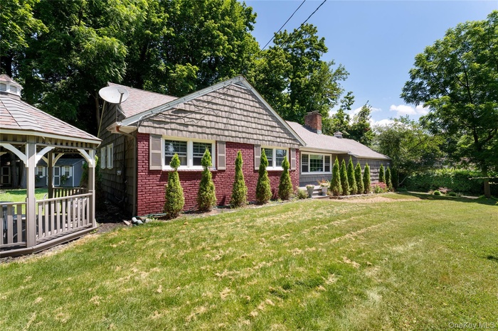 View of front of home featuring a front yard, a gazebo, a chimney, and brick siding