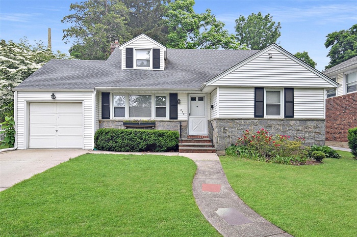 View of front facade with stone siding, a front lawn, a shingled roof, entry steps, and a garage