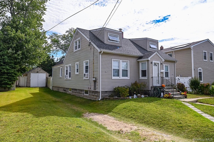 View of front of home with a storage unit, a front lawn, a shingled roof, and a chimney