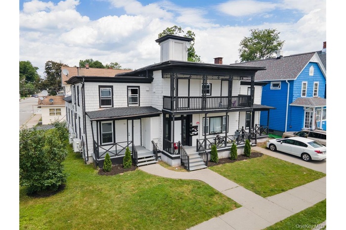 View of front of property with a chimney, a porch, a balcony, a front yard, and roof with shingles