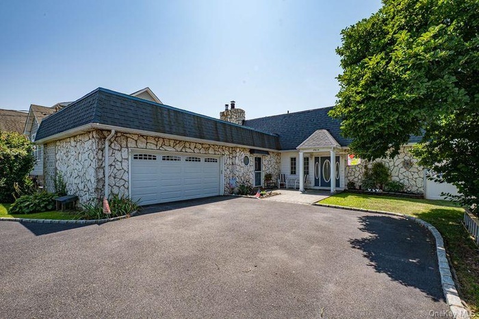 View of front of house featuring asphalt driveway, a shingled roof, an attached garage, and a chimney