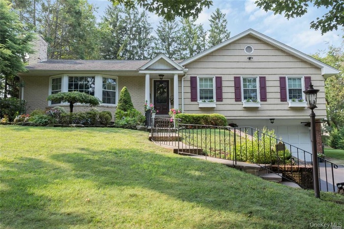 View of front of home featuring brick siding, a chimney, an attached garage, and a front lawn