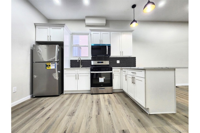 Kitchen featuring stainless steel appliances, tasteful backsplash, a peninsula, white cabinetry, and light wood-type flooring