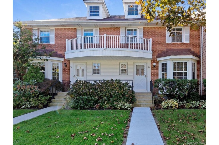 View of front of house with a balcony, a front lawn, and brick siding
