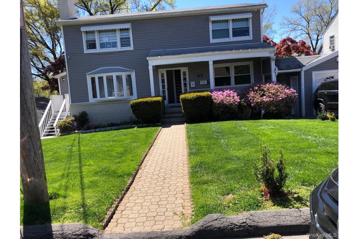 View of front facade with brick siding, a porch, a chimney, and a front yard