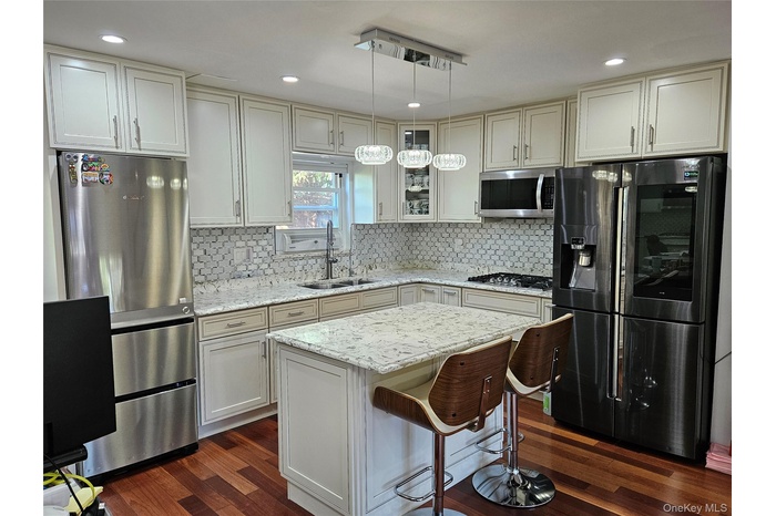 Kitchen featuring appliances with stainless steel finishes, glass insert cabinets, light stone counters, hanging light fixtures, and a breakfast bar a