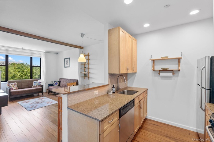 Kitchen featuring light stone counters, open floor plan, light wood-style flooring, backsplash, and beamed ceiling