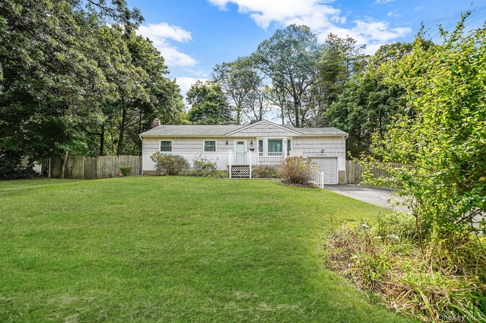 Ranch-style house with a garage, driveway, view of wooded area, and a chimney