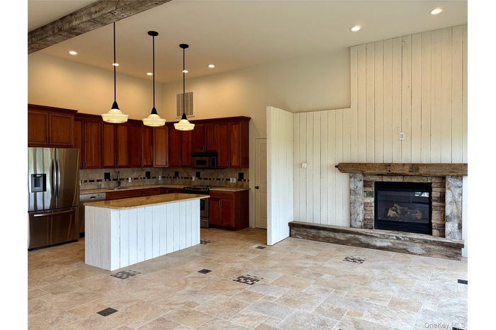 Kitchen featuring stainless steel appliances, a towering ceiling, tasteful backsplash, pendant lighting, and brown cabinetry