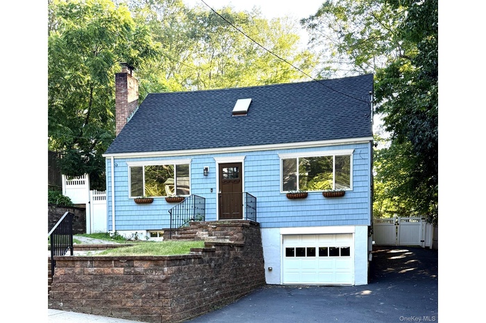 View of front of property featuring an attached garage, a chimney, driveway, and roof with shingles