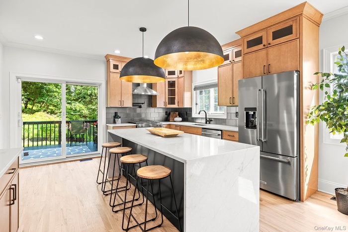 Kitchen featuring decorative backsplash, a kitchen breakfast bar, appliances with stainless steel finishes, light wood finished floors, and crown mold