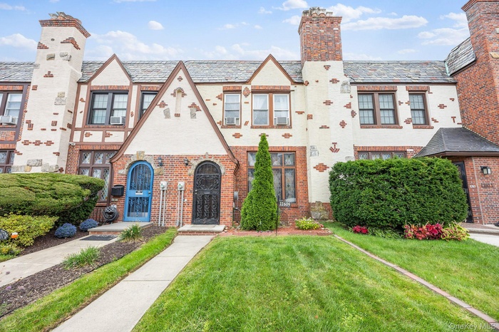 Tudor-style house with a high end roof, a front yard, a chimney, and brick siding