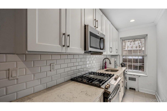 Kitchen with white cabinetry, appliances with stainless steel finishes, radiator, and sink