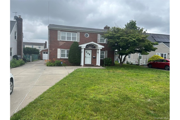 View of front of property with brick siding, a front yard, a garage, concrete driveway, and a chimney