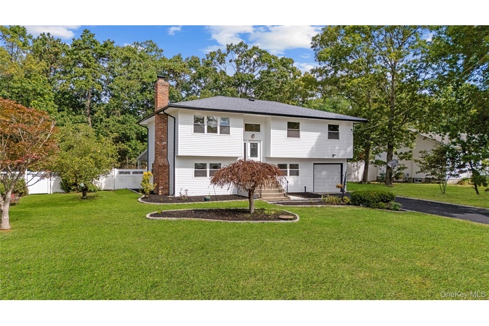 Split foyer home with a chimney, view of scattered trees, and asphalt driveway