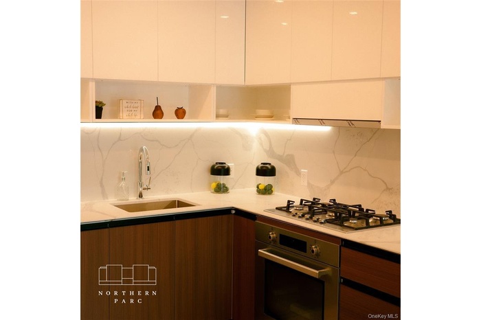 Kitchen featuring modern cabinets, stainless steel appliances, backsplash, and light stone counters