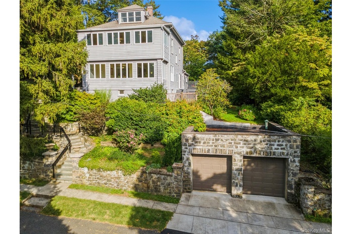 Front view of the house with 2 car garage, view of landscaping, and cedar and stone siding