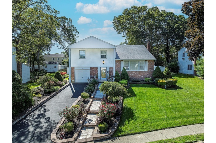 View of front facade featuring brick siding, driveway, a garage, a chimney, and a front lawn