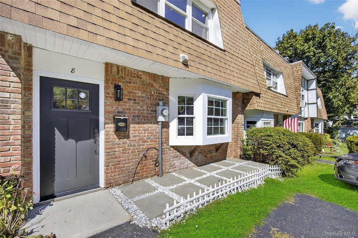 Property entrance featuring mansard roof, brick siding, and roof with shingles