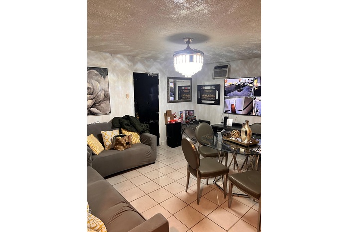 Living room featuring a wall mounted AC, light tile patterned floors, and a textured ceiling