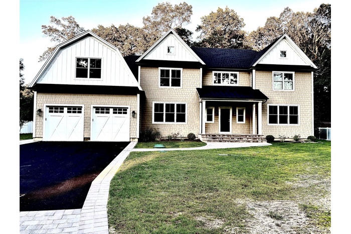 View of front of house with a gambrel roof, covered porch, a garage, asphalt driveway, and a front lawn