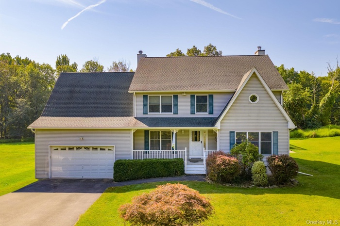 Traditional home with a porch, a front lawn, asphalt driveway, and roof with shingles