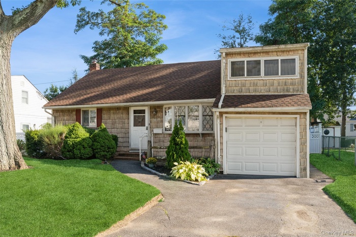 View of front facade with a chimney, a shingled roof, and a garage