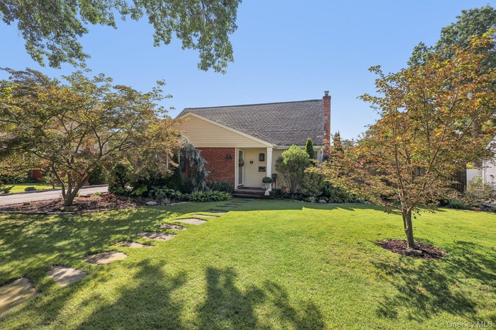 View of front of house with a front yard, brick siding, a chimney, covered porch, and a shingled roof