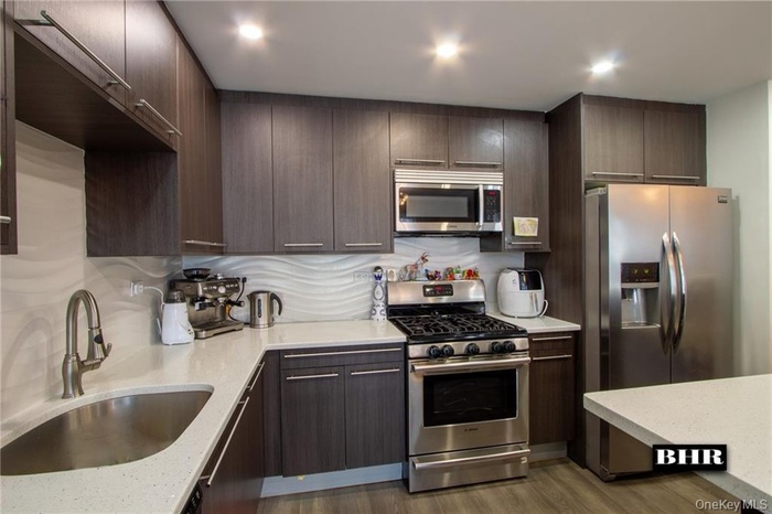 Kitchen with appliances with stainless steel finishes, light stone countertops, dark wood-style floors, modern cabinets, and dark brown cabinets