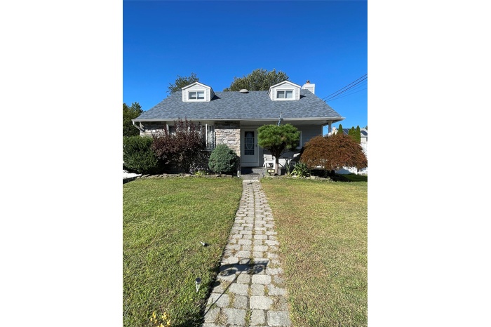 Expanded Cape-style house featuring a shingled roof, a front lawn, a porch, and a chimney