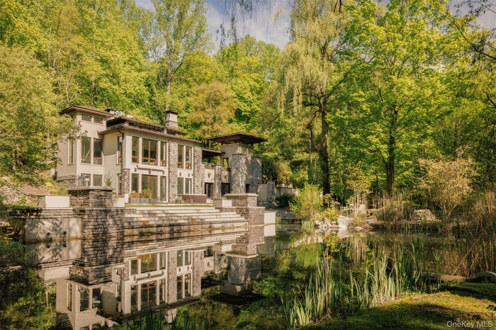 View of side of home featuring a chimney, stone siding, stucco siding, and a balcony
