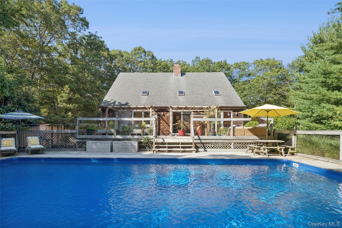 View of pool with a pergola, a wooden deck, view of wooded area, and a patio